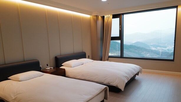 A hotel room with two beds, a nightstand, and a large window offering a mountain view.