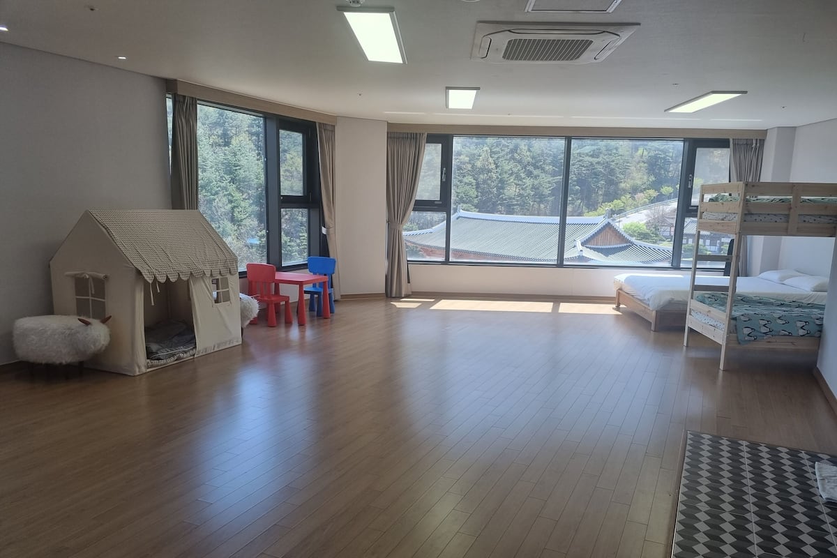 A spacious room with a wooden floor, a bunk bed, a playhouse, and a table with chairs.