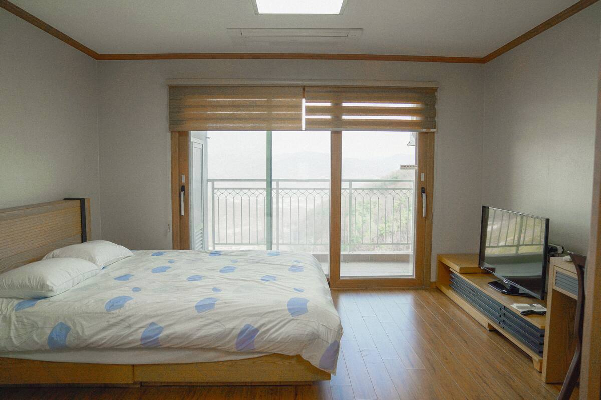 A bedroom with a bed, a television, and a sliding glass door leading to a balcony.