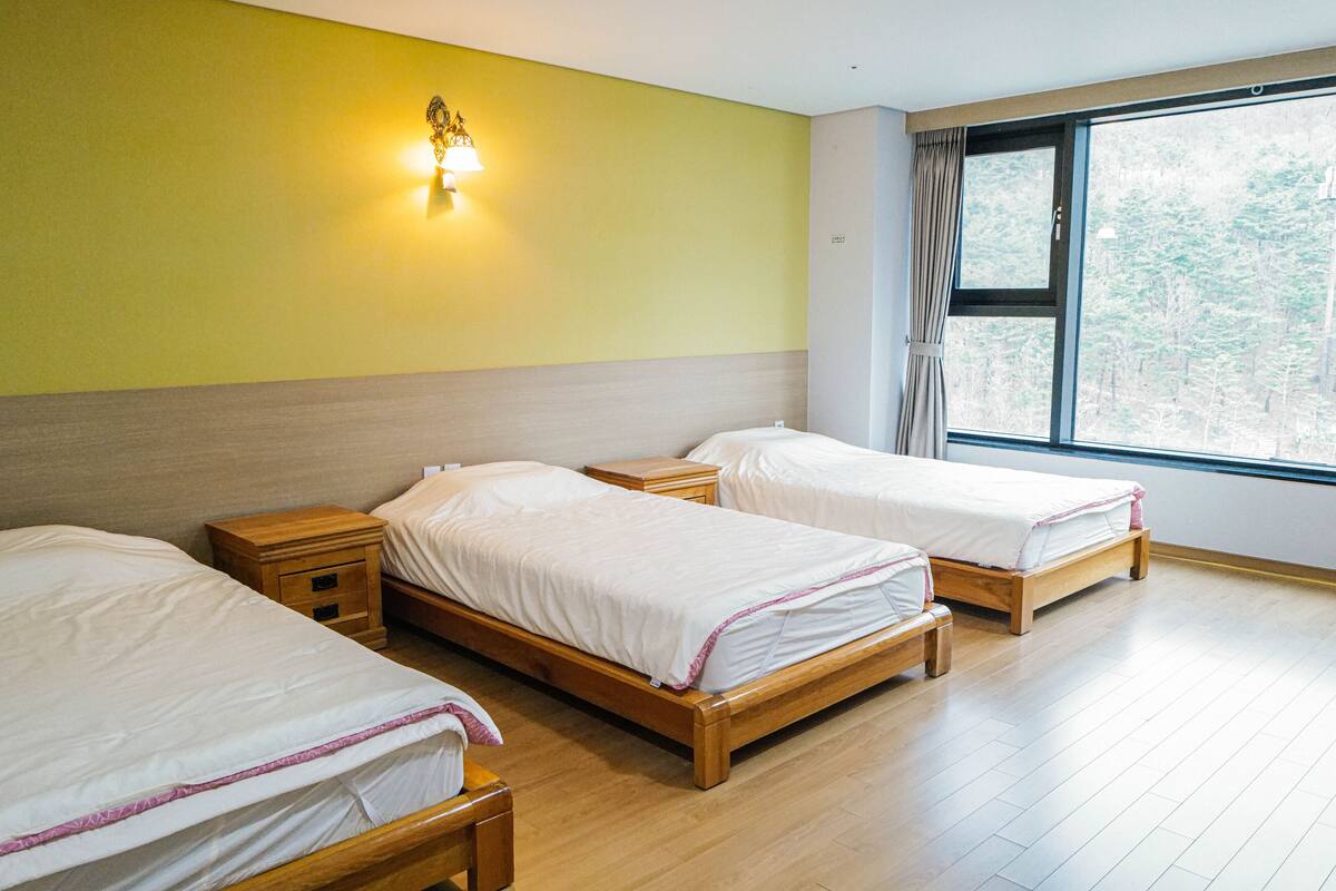 A room with three wooden beds, a nightstand, and a wall-mounted lamp.