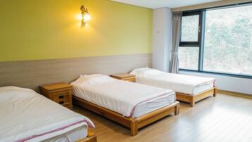 A room with three wooden beds, a nightstand, and a wall-mounted lamp.