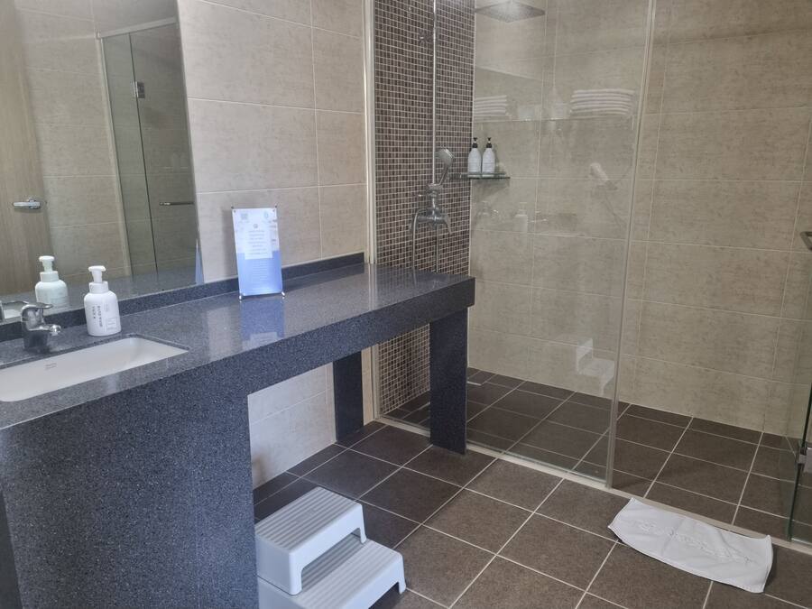 A modern bathroom with a granite countertop, a glass shower enclosure, and a tiled floor.