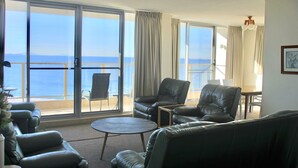 Een kamer met uitzicht op zee, met een bank, twee fauteuils, een klein rond tafeltje en een stoel bij het raam.