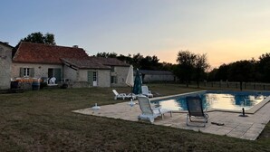 Ein Garten mit Pool, überdachter Terrasse und einem rustikalen Haus.