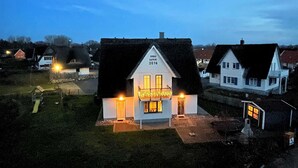 Un edificio blanco con techo oscuro, un letrero iluminado y un pequeño porche.