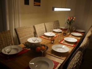 Une table à manger dressée avec des assiettes, des verres et un centre de table composé de fleurs et de fruits.