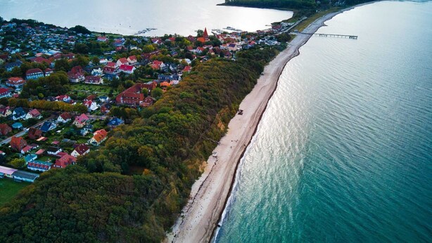 Vista aérea de un pueblo costero con playa, casas y un puente.