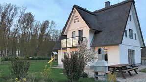 Una casa con techo de paja, un balcón y una mesa de picnic.