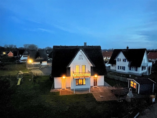 A white building with a dark roof, a lit sign, and a small porch.