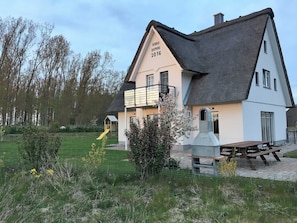A house with a thatched roof, a balcony, and a picnic table.