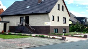 A two-story building with a brick facade, a sloped roof, and a small porch with steps. - Groot Huus Horumersiel OG rear - Groot Huus upper floor for max. 4 persons (Wangerland)