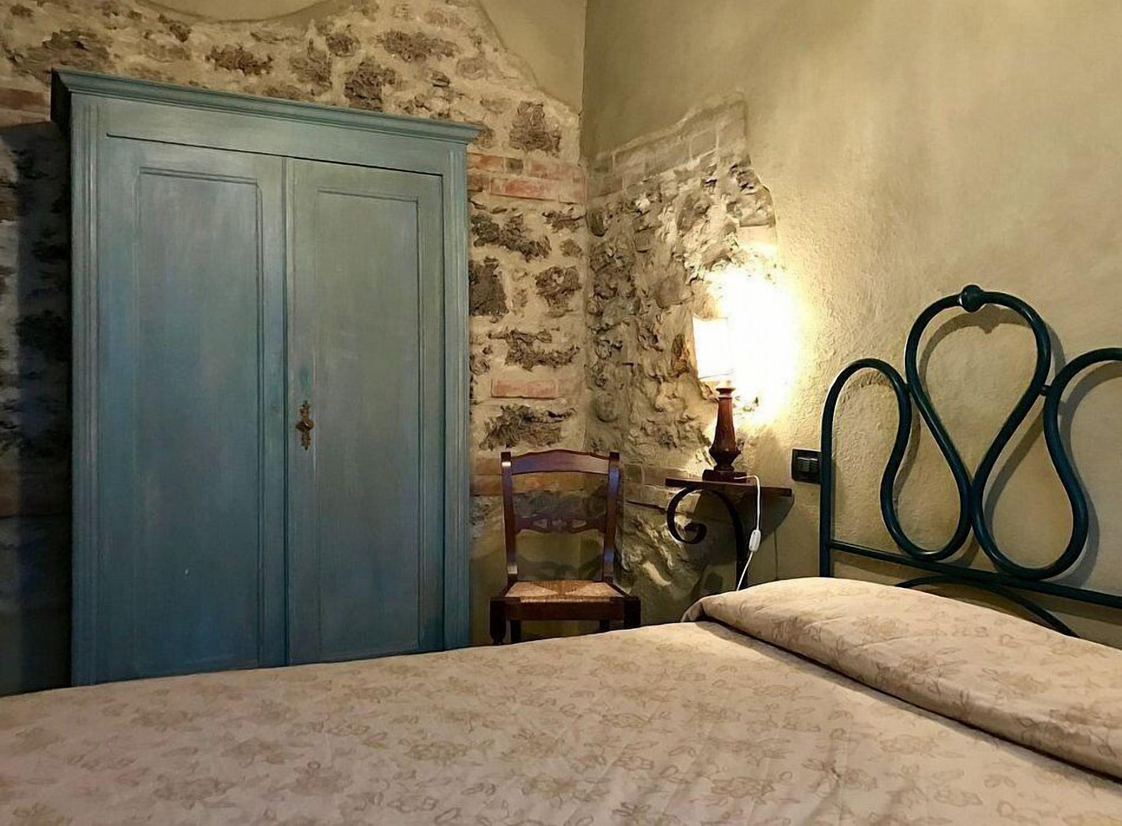 Quarto com cama, uma cadeira, guarda-roupa e luminária na parede.