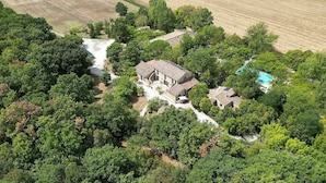 An aerial view of a property with multiple buildings surrounded by dense greenery, a visible swimming pool, and a small waterfall.