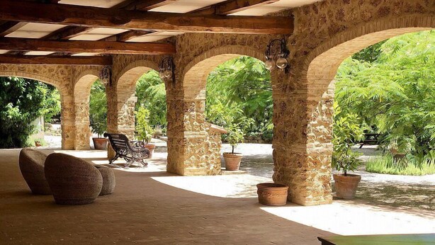 A covered outdoor area with stone arches, potted plants, and seating.