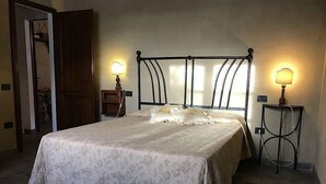 Ein ordentlich bezogenes Bett mit einer blumigen Tagesdecke, zwei Nachttischlampen und eine Holztür im Hintergrund.