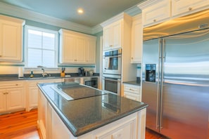 A modern kitchen with white cabinetry, stainless steel appliances, and a granite countertop. - Luxury Home in Gated Community; 3 Minute Walk to Beach; Access to Oceanside Community Pool & Cabana (Isle of Palms)