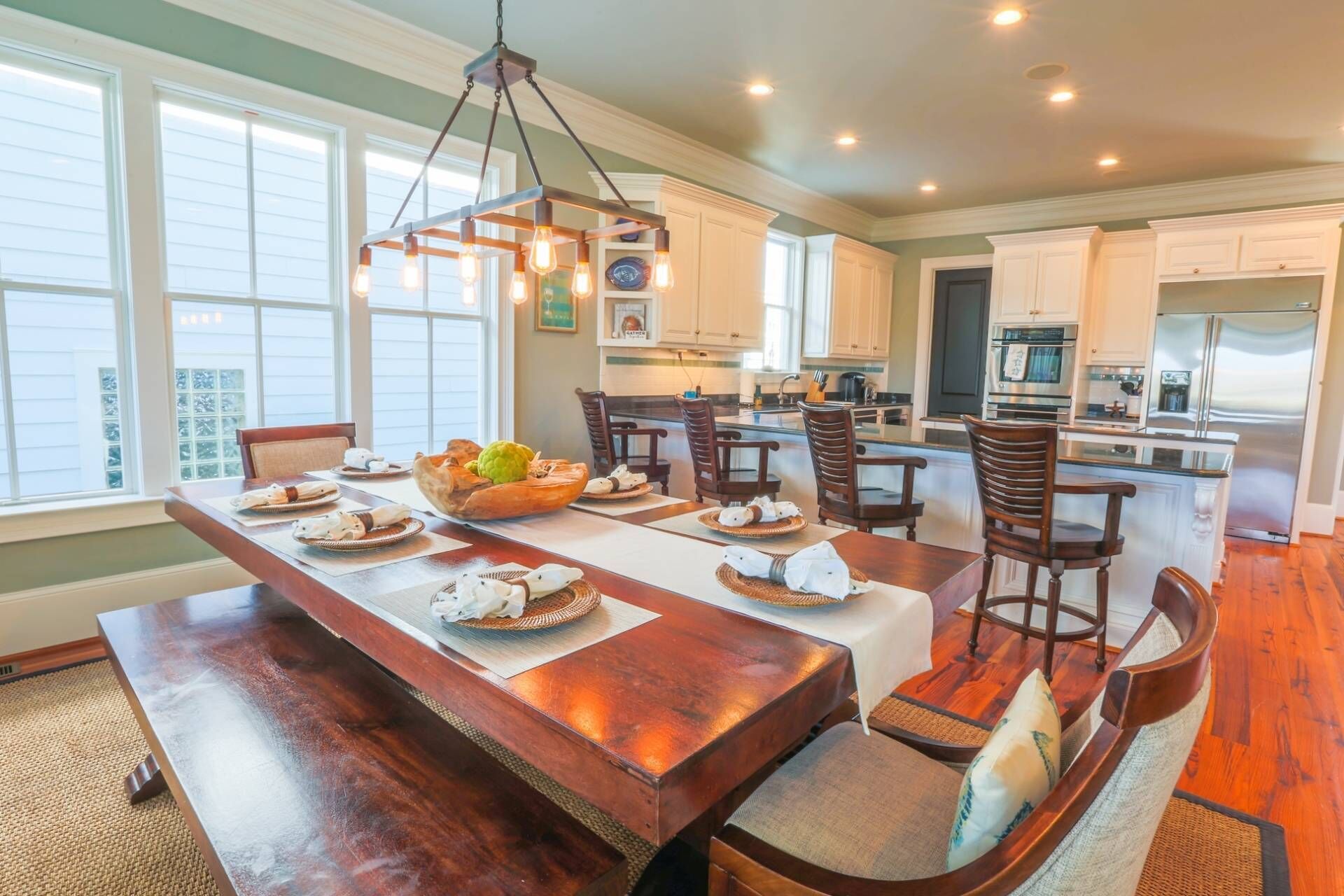 A spacious dining area with a long wooden table, multiple chairs, and a hanging light fixture.