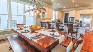A spacious dining area with a long wooden table, multiple chairs, and a hanging light fixture.