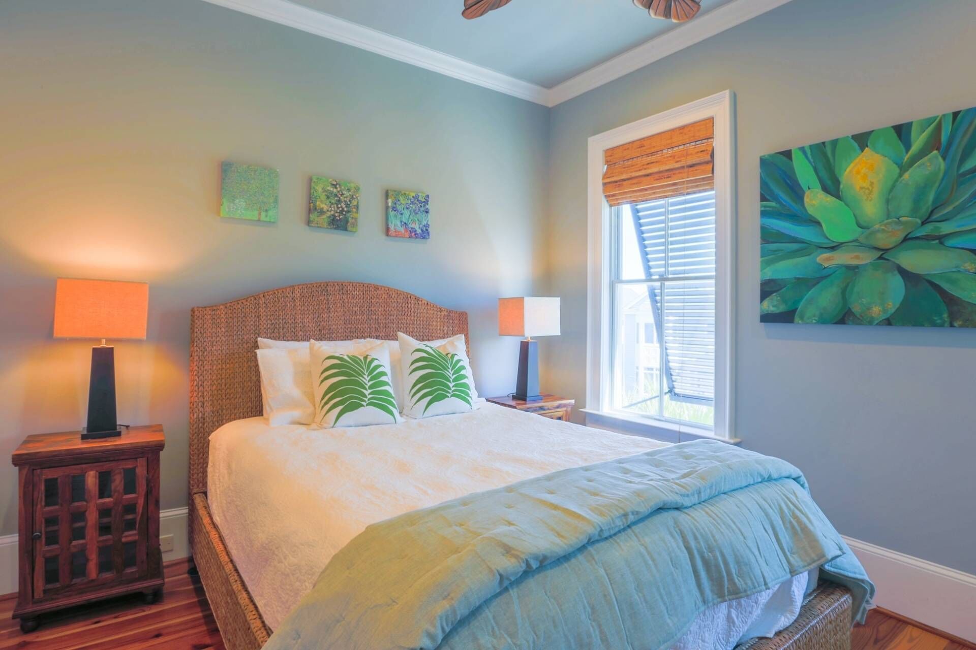 A bedroom with a large bed, two bedside tables with lamps, a window with blinds, and three wall art pieces.