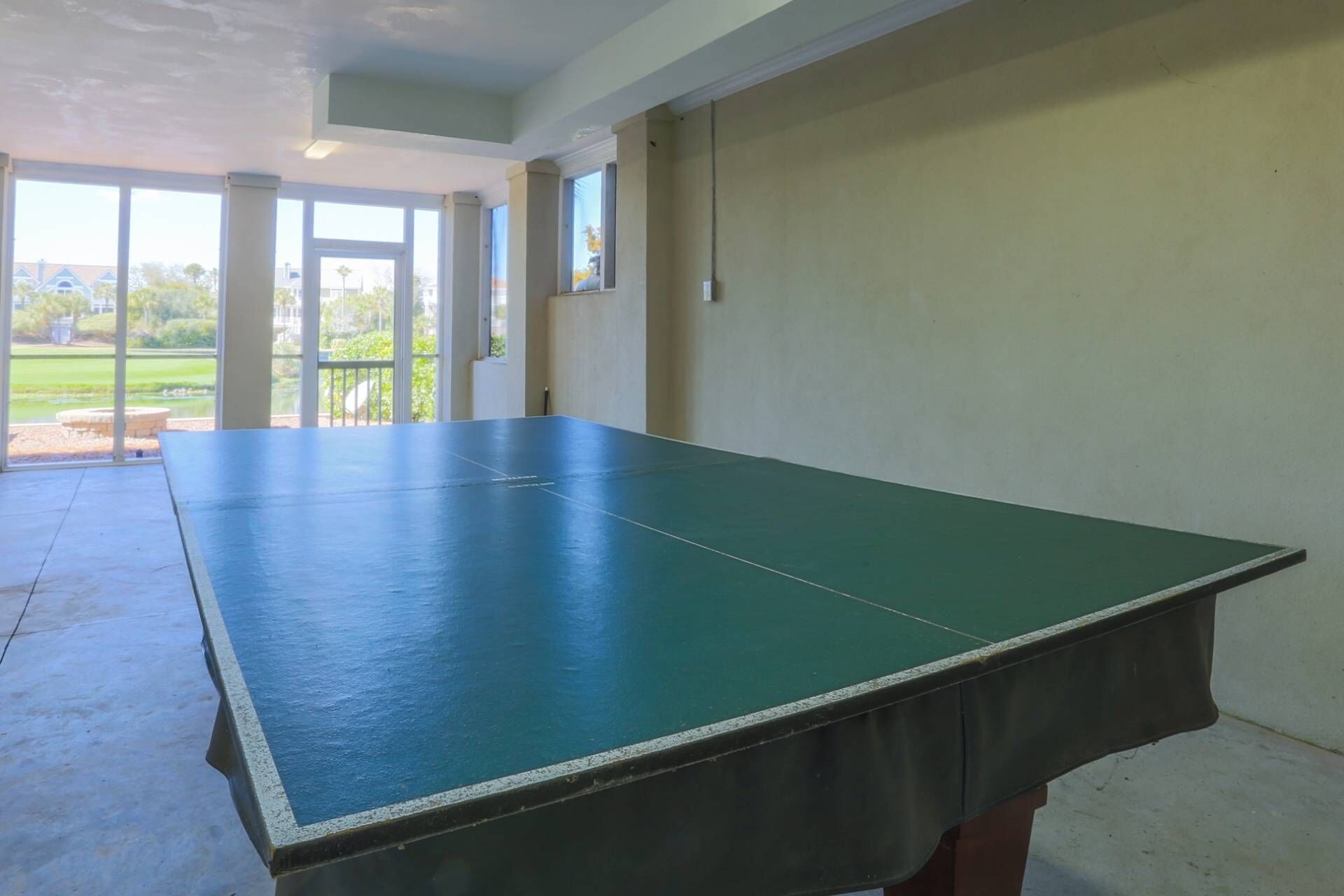 A ping pong table in a room with large windows and a view of a green landscape.