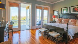 A bedroom with a large bed, two bedside tables, a nightstand, a chair, and a balcony with a view.