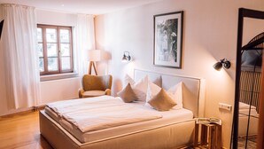 Un dormitorio con una cama grande, una silla, una lámpara, un cuadro enmarcado y un radiador.