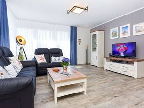 Un salon avec un canapé, une table basse, un téléviseur et des œuvres d’art accrochées au mur.