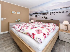 A bedroom with a bed, nightstands, a dresser, a wall-mounted lamp, and a beach-themed mural.