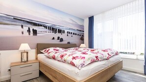 A bedroom with a bed, nightstands, a wall mural, and a window with curtains. - Ferienwohnung Schlipf in Carolinensiel - Ferienwohnung Schlipf (Wittmund)