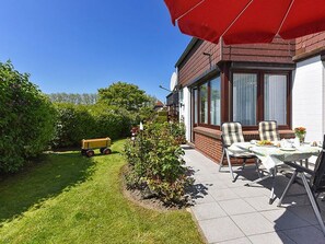 Une terrasse avec une table et des chaises, un parasol rouge et un petit jardin.