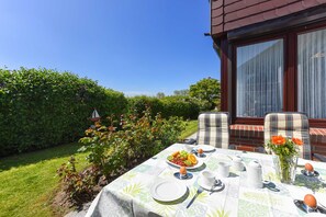 Une table à manger installée à l’extérieur, avec des assiettes, des tasses et un vase rempli de fleurs, entourée de chaises et offrant une vue sur le ciel.