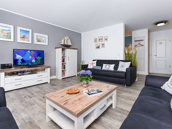 A modern living room with a flat-screen TV, a wooden coffee table, a black sofa, and a bookshelf.