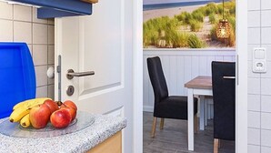 A kitchen with a view of a beach, a dining area with chairs, and a fruit bowl on the counter. - Ferienwohnung Schlipf in Carolinensiel - Ferienwohnung Schlipf (Wittmund)