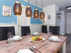 Un coin repas avec une table en bois dressée pour quatre personnes, entourée de chaises noires, sous des suspensions décoratives.