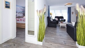 A modern living room with a sofa, a coffee table, and a TV. There is a bed with a view of the sea in the background. - Ferienwohnung Schlipf in Carolinensiel - Ferienwohnung Schlipf (Wittmund)