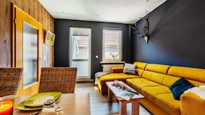 Een gezellige woonkamer met een gele bank, een houten eettafel en een rieten stoel.