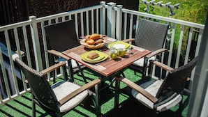 Een houten tafel met stoelen, een broodmand en een bord eten op een balkon met een witte balustrade.