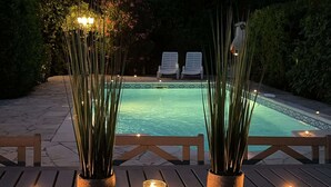Ein Poolbereich mit zwei Liegestühlen, einer Holzterrasse und hohen Pflanzen in gewobenen Körben.