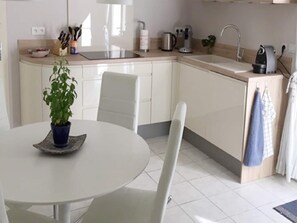 A modern kitchen with white cabinetry, a sink, and a dining area with a round table and chairs. - Villa in Saint-Couat with Private Pool (Saint Couat d'Aude)