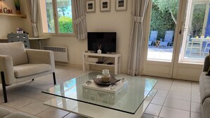 Ein Wohnzimmer mit einem Glastisch, zwei Sofas, einem Fernseher auf einem Schrank und Blick ins Freie durch große Fenster.