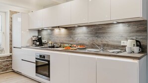 A modern kitchen with white cabinets, a wooden backsplash, and stainless steel appliances. - Bergwald - Ferienwohnung Bergwald (Braunlage)