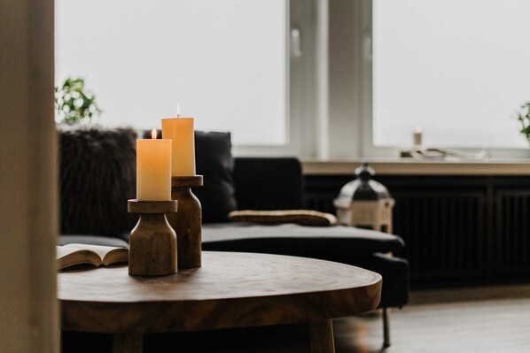 A wooden table with two candles, a book, and a window in the background.