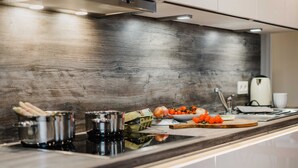 A modern kitchen with a wooden backsplash, stainless steel appliances, and a variety of fresh produce on the counter. - Bergwald - Ferienwohnung Bergwald (Braunlage)