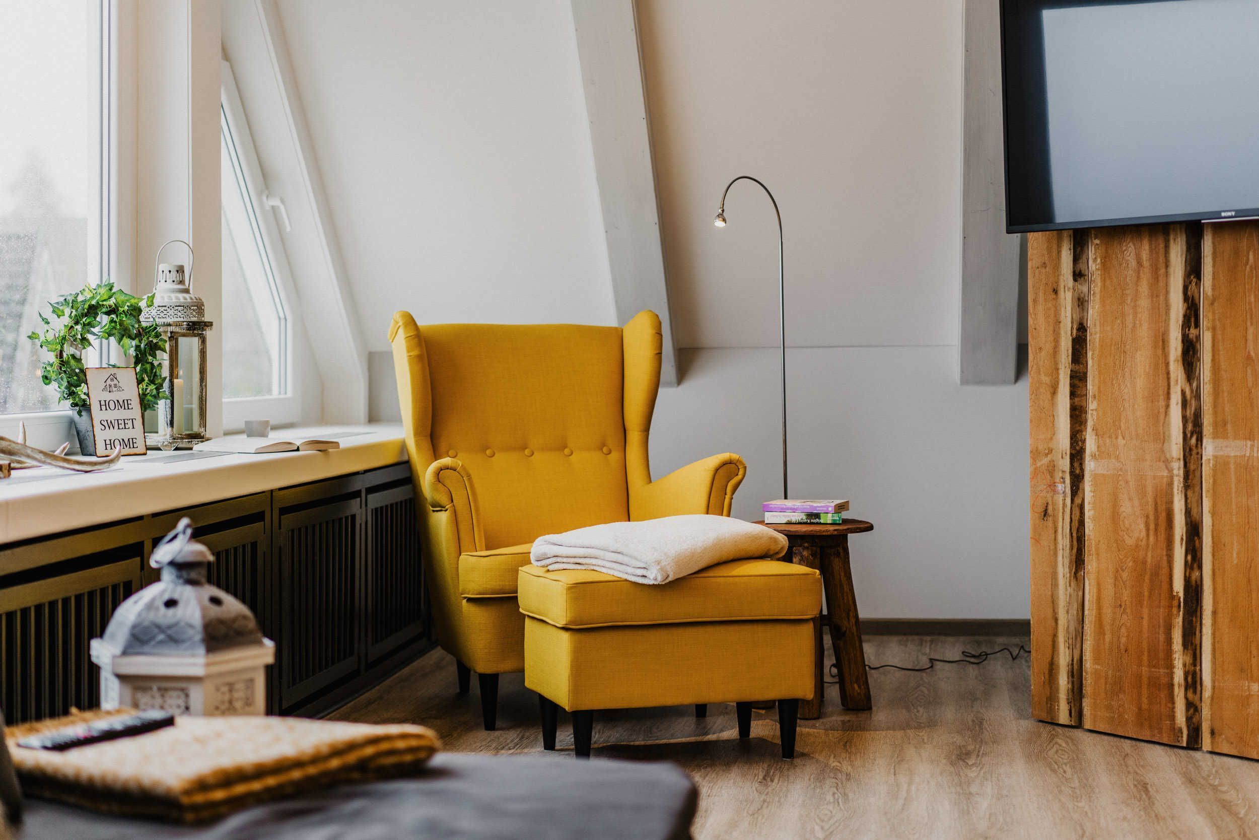 A room with a yellow armchair, a small wooden side table, a television, and a radiator.