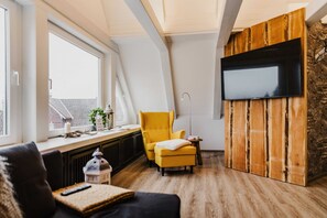 A modern living room with a yellow armchair, a black sofa, a mounted TV, and a stone wall. - Bergwald - Ferienwohnung Bergwald (Braunlage)