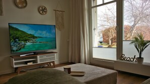 A living room with a television, a coffee table, and a window with a view of trees and a car. - Arkona Beach, Deutschland (Breege)