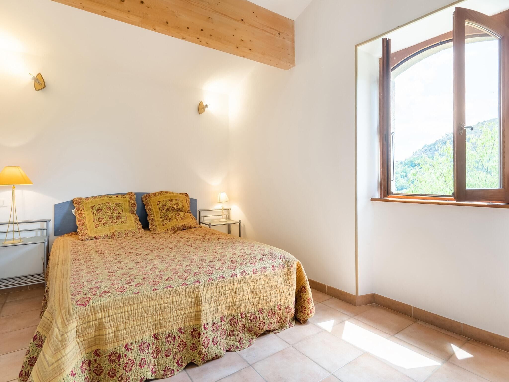 Ein Schlafzimmer mit einem Bett, zwei Nachttischlampen, einem Fenster und einer Holzbalkendecke.