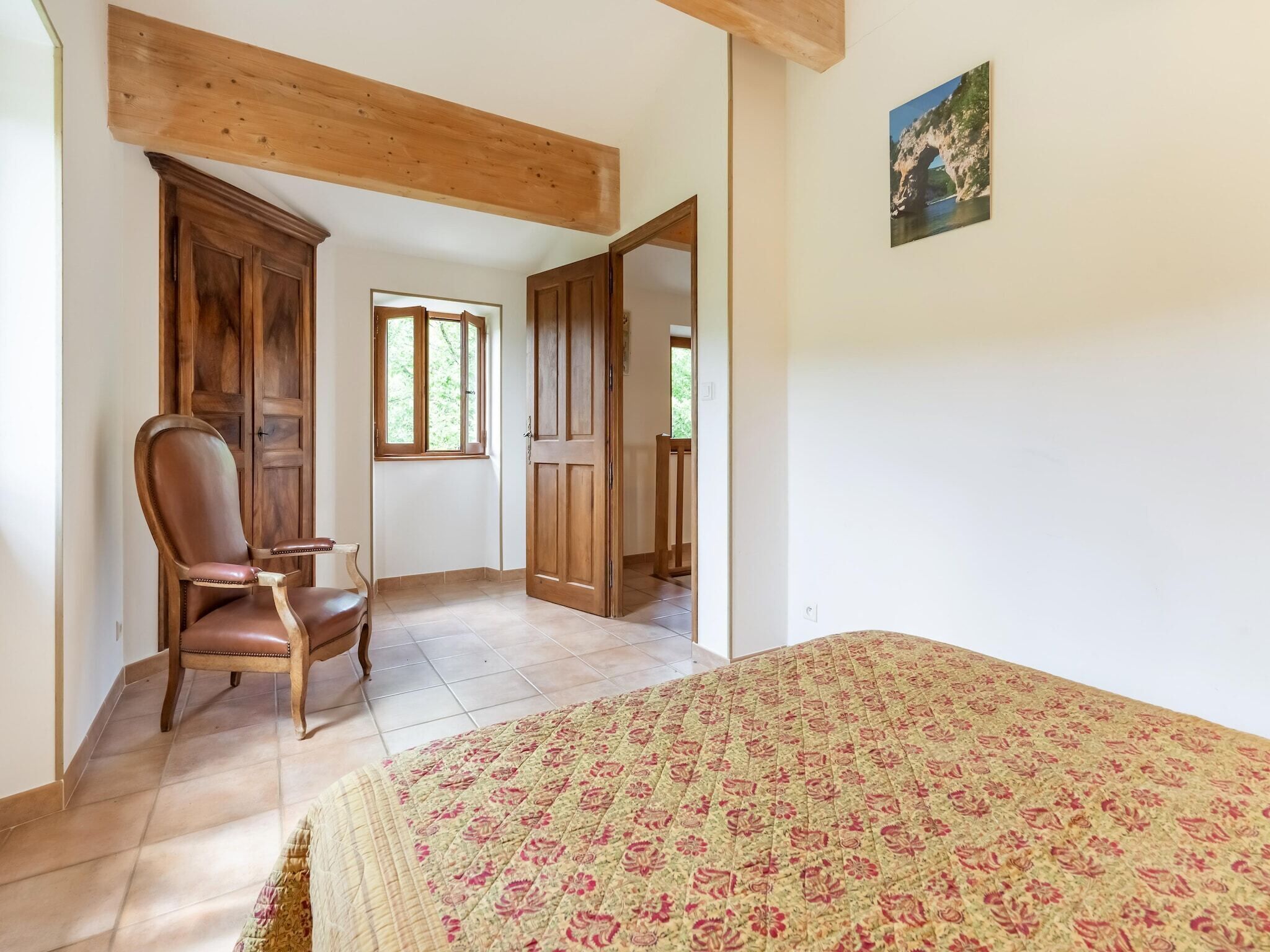 Een slaapkamer met een houten bed, een stoel, een kledingkast en een raam.