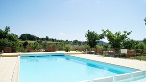 Une piscine rectangulaire, bordée d’une terrasse carrelée, entourée d’une clôture et de verdure.