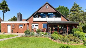 A two-story building with a red brick facade, a balcony with blue umbrellas, and a well-maintained garden. - Ferienwohnung Haus Heimathafen (Esens)